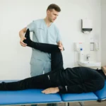 A physiotherapist assists a patient with leg stretching exercises on a treatment table.